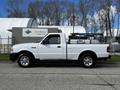 A white 2010 Ford Ranger pickup truck with silver wheel rims parked on a road featuring a flatbed with a rack on the back