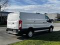 A side view of a white 2017 Ford Transit van with a black stripe near the bottom and silver alloy wheels parked on a street