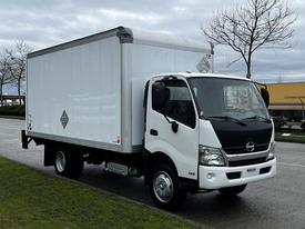 A 2019 Hino 195 truck with a white box-shaped cargo area and a black front cab parked on a roadside
