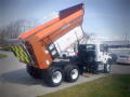A 2016 International WorkStar 7500 dump truck with an orange bed raised, revealing a white compartment and black chassis, parked on the side of a street