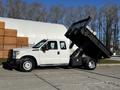 A 2011 Ford F-350 SD with a dump bed raised, showcasing its capabilities as a heavy-duty work truck with a white exterior and dual rear wheels