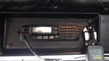 A black communication radio with buttons labeled P1 P2 P3 mounted on a textured surface inside a vehicle