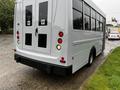 A white 2015 Chevrolet Express shuttle bus with a flat rear design and large windows for passengers with two doors and wheelchair accessibility features