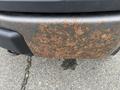 A close-up of a rusty rear bumper on a 2010 Ford F-150 showing significant corrosion and wear