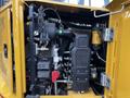 The image shows the engine compartment of a 2024 Caterpillar 306 with various components including a black housing unit a yellow filter and cabling attachments