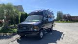 A 2013 Ford Econoline van with a raised roof and a metal rack on top parked on a concrete surface