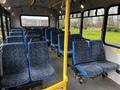 Interior of a 2017 Chevrolet Express bus featuring multiple blue fabric seats with a patterned design and a yellow support pole in the aisle
