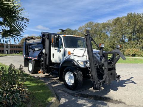 A white 2007 International 7300 truck equipped with a dark blue refuse body and hydraulic lift arms in the front