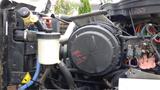 Close-up of the engine compartment of a 2012 International 7400 featuring various hoses a coolant reservoir and an air filter housing