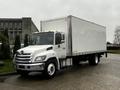 A 2020 Hino 338 box truck with a white cargo area and front grille featuring a distinctive logo positioned at an angle