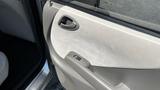 Close up of the inside door panel of a 2006 Honda Fit featuring a beige fabric texture and a small door handle with a power window control