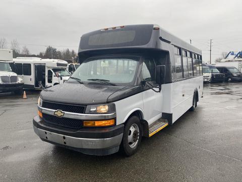 2018 Chevrolet Express bus with a white body and black front grille parked at a lot with large windows and a wheelchair ramp on the side