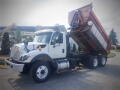 A 2016 International WorkStar 7500 dump truck with a white cab and a raised orange dump bed showing the truck's hydraulic lifting mechanism