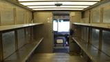 Interior of a 2011 Ford Econoline with metal shelves on both sides and a view of the driver's seat and dashboard at the front