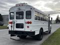 A white 2013 International 4200 bus featuring large windows and a step at the rear with red and amber lights visible on the back