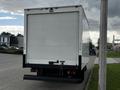 A white 2022 Isuzu NPR truck with a closed rear box and visible tail lights parked on a street.