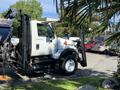 A white 2007 International 7300 truck with a black and silver hydraulic arm attachment on the side