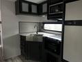 Interior view of a 2022 Aspen Trail featuring a kitchen area with dark cabinetry a stainless steel sink and appliances including a microwave and stove