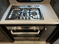 A stainless steel gas stove with four burners and an oven below on a light countertop inside a recreational vehicle