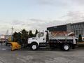 A 2006 Freightliner M2 106 dump truck with a yellow snow plow attached to the front