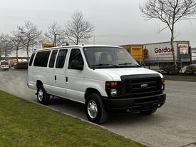 A white 2011 Ford Econoline van with sliding side doors and multiple windows