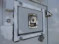 A metallic access panel with a latch and a small handle on the side of a gray vehicle