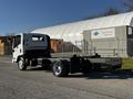 A white 2017 Isuzu NQR truck chassis with a simple cab and no cargo in the back, parked with a warehouse in the background