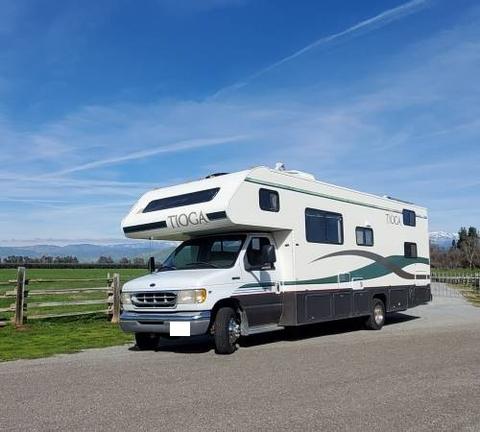 A 1998 Fleetwood Tioga Bunkbed motorhome with a white and green exterior parked on a gravel road