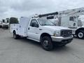 A white 2003 Ford F-450 SD truck with a flatbed and utility boxes on the sides parked on a lot