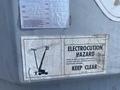 A warning sign on a Genie S-65 4X4 showing an illustration of a person near a raised platform with a caution about electrocution hazard and instructions to keep clear