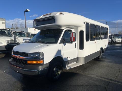 A 2012 Chevrolet Express bus with a white exterior and large windows parked at a dealership