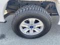 A close-up of a silver alloy wheel and tire of a 2017 Ford F-150 showing the tread pattern and the Ford logo on the hubcap