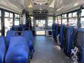 Interior of a 2020 Chevrolet Express showing blue seating arranged in rows with an open aisle leading to the front and large windows on the sides