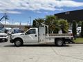 A white 2015 Ford F-350 SD flatbed truck parked with palm trees in a wooden bed and a storage compartment on the side