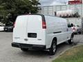 A white 2018 GMC Savana van with a high roof and rear doors, parked with chrome wheels and no visible license plate