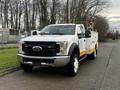 A white 2019 Ford F-550 truck with an orange and yellow stripe and a utility bed parked on the street