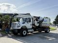 A white 2013 International 7400 truck equipped with a large vacuum tank and multiple hoses attached for industrial cleaning purposes