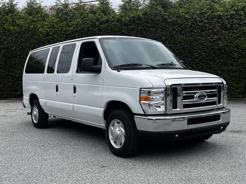 A white 2008 Ford Econoline van with a chrome grille and multiple side windows parked on a surface with a textured appearance