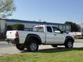 A white 2015 Toyota Tacoma pickup truck parked with a double cab and spacious bed shown from a side angle