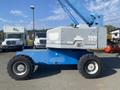 A blue 1997 Genie S-65 4X4 aerial lift with wide tires and a raised boom arm
