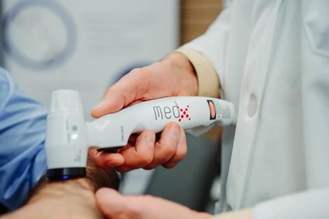 A person holds a deep tissue laser device with a white body and a red logo near a patient's arm demonstrating a therapeutic treatment