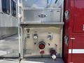 Close-up of a fire truck's pump panel featuring valves hoses and gauges indicating water flow and pressure with a central control marked by a red circular emblem