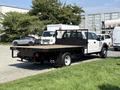 A white 2018 Ford F-550 flatbed truck with a black flatbed and a mesh rear gate is parked on a grassy area