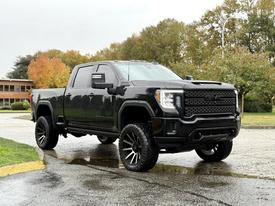 A black 2022 GMC Sierra 3500HD with a lifted suspension large tires and a bold front grille parked on a wet surface
