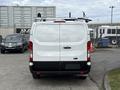 A 2023 Ford Transit van viewed from the rear with a white body and black lower panel featuring a ladder rack on top