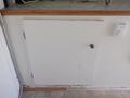 A white cabinet door with a round knob on the front of a trailer interior, showing some wear along the edges and surface