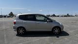 A silver 2006 Honda Fit parked in a lot with a side profile view showcasing its compact design and sporty wheels