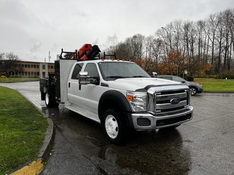 A 2014 Ford F-550 with a flatbed and equipment rack on the back is parked at an angle on a wet road