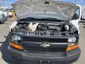 A 2013 Chevrolet Express van with its hood raised, revealing the engine compartment and various engine components in view