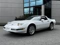 A 1992 Chevrolet Corvette in white with a convertible top and distinctive pop-up headlights parked in front of a building